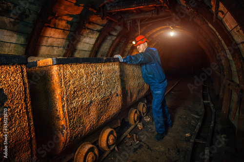 A miner in a coal mine stands near a trolley. Copy space.