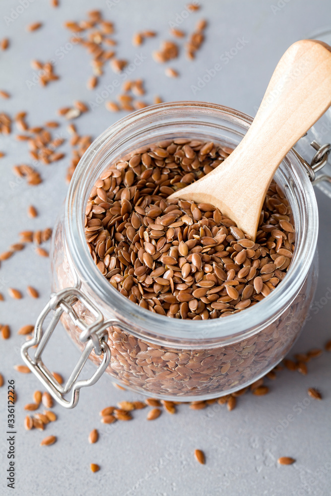 flax seeds in glass jar with wooden spoon on blue background flax seeds in glass jar with wooden spoon on blue background