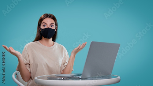woman put her hands a sight in a surprise, she use her computer and wear black medical mask