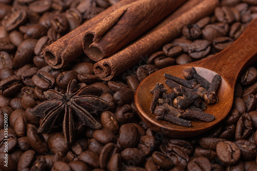 Sticks of cinnamon, anise and cloves in a wooden spoon against the background of coffee beans