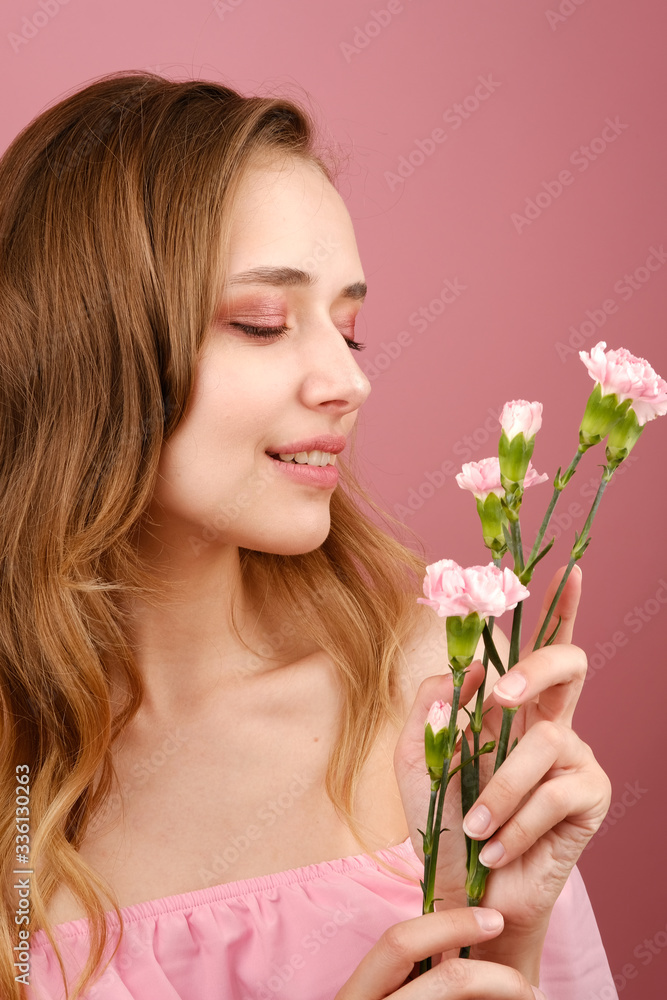 Close-up beauty portrait of an attractive young woman in a summer dress holding a carnation flower in her hand. A girl with light wavy hair. Isolated on a pink background Close-up beauty portrait of an attractive young woman in a summer dress holding a carnation flower in her hand. A girl with light wavy hair. Isolated on a pink background