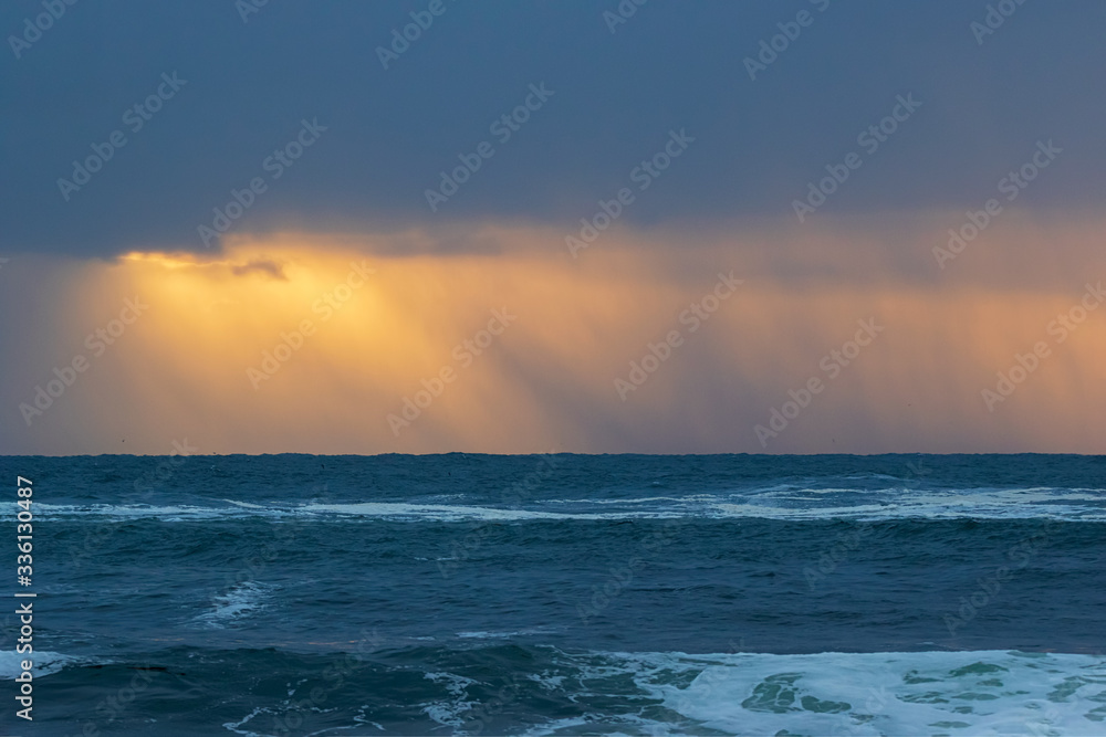 Obraz premium A rainstorm over the ocean with beautiful orange sky 