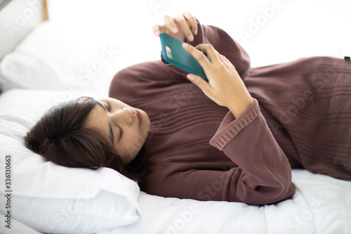 Asian woman watching media from phone in a bedroom in her bedroom feeling lonely. The concept of daily activities of people in the capital and housewives.