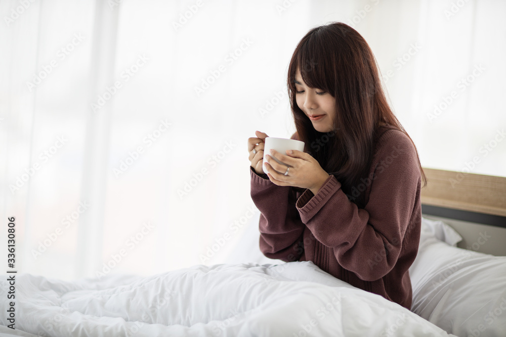 Asian woman smiling and holding cup of coffee in her bedroom. corovavirus covid-19, stay at home, work form home concept. Asian woman smiling and holding cup of coffee in her bedroom. corovavirus covid-19, stay at home, work form home concept.