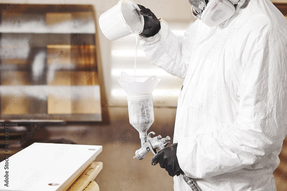 Obraz premium Man pours paint into the sprayer before painting the wood.
