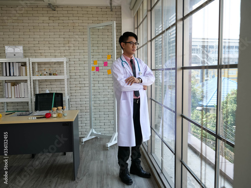 Male doctor of an Asian nutritionist stands to relax and enjoy the view by the window.