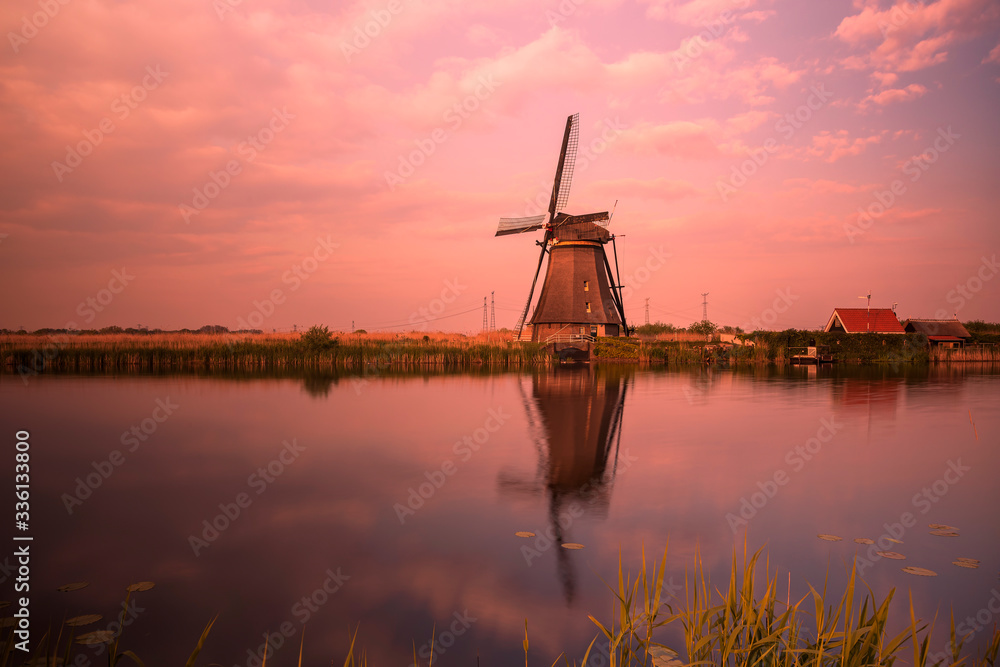 A windmill by a canal in Kinderdijk Holland is reflected in the water.