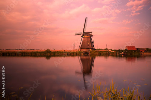 A windmill by a canal in Kinderdijk Holland is reflected in the water.