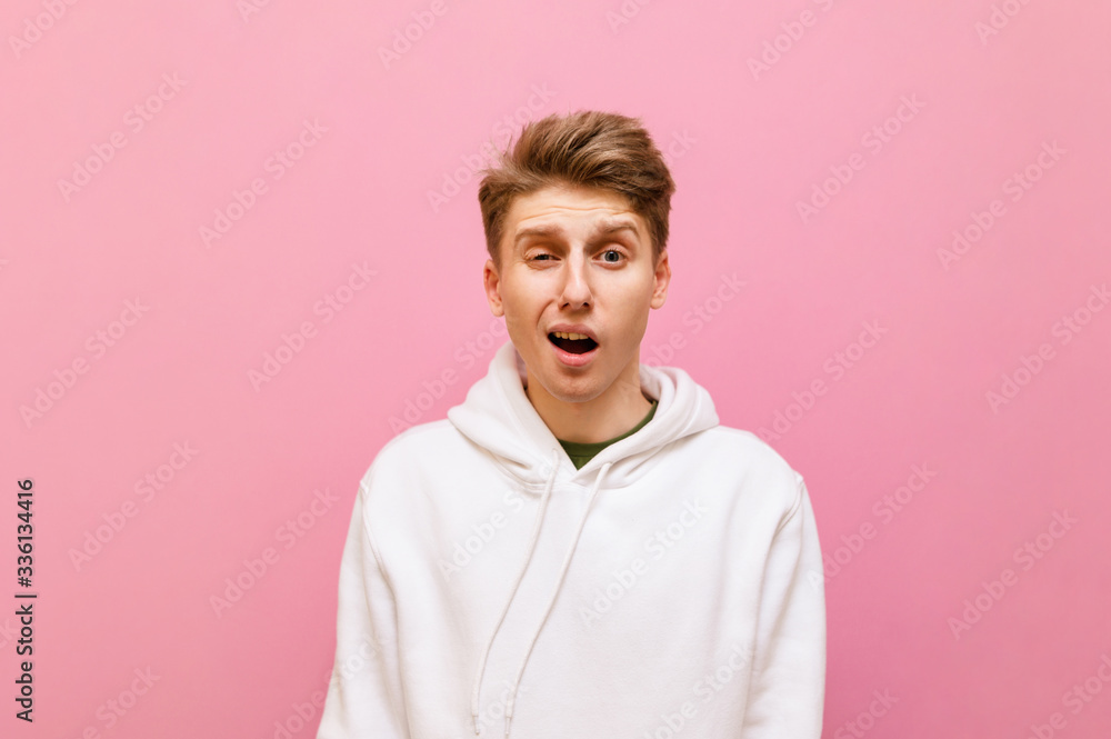 Funny young blond man in white sweatshirt isolated on pink background looking into camera with shocked funny face. Suspicious guy on a pink background. Copy space Funny young blond man in white sweatshirt isolated on pink background looking into camera with shocked funny face. Suspicious guy on a pink background. Copy space