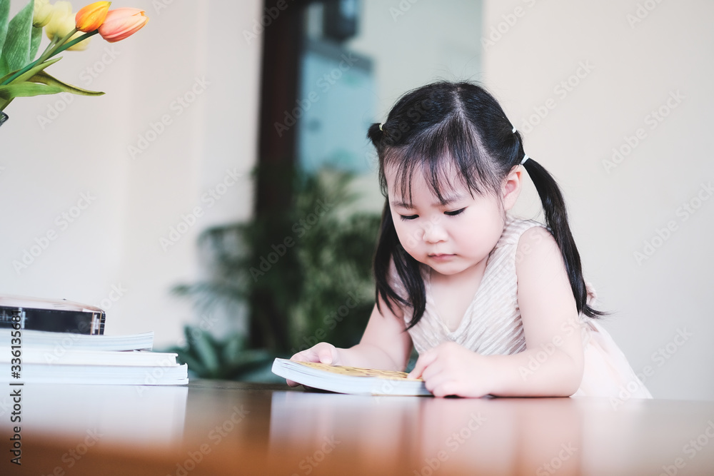 Cute asian girl learning by reading and studying books and playing at home in the living room sitting, home schooling education for children, feeling happy cheerful, and enjoying staying at home