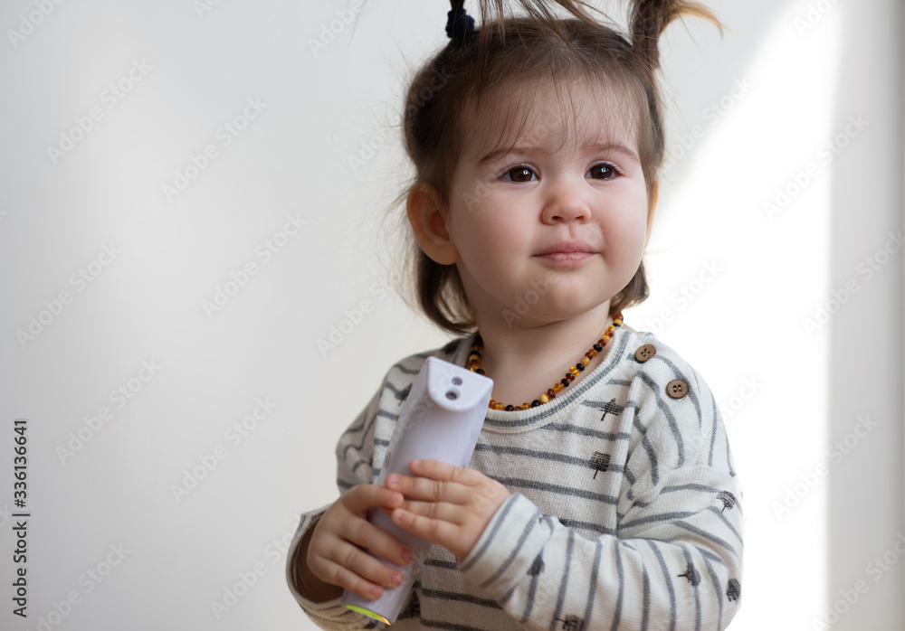 Pretty little newborn baby girl playing with electronic thermometer. Pretty little newborn baby girl playing with electronic thermometer.