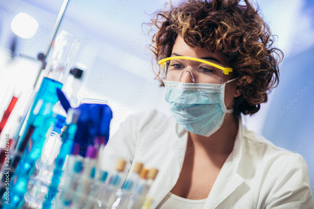 Fototapeta premium Young attractive female scientist in protective eyeglasses and gloves using test tube with blue liquid sample substance probe in the scientific chemical research laboratory