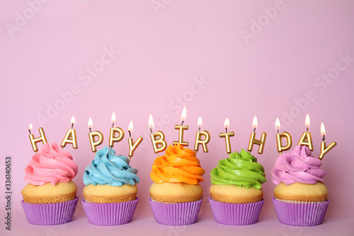 Birthday cupcakes with burning candles on pink background. Space for text