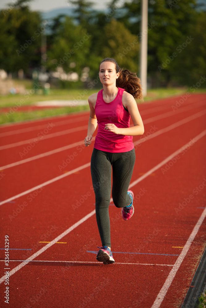 Beautiful young woman runner run on a track in early summer afternoon Beautiful young woman runner run on a track in early summer afternoon