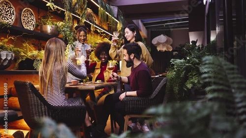  A group of friends from various ethnic groups enjoy happily and toast in a restaurant and bar with a very careful and elegant decoration
