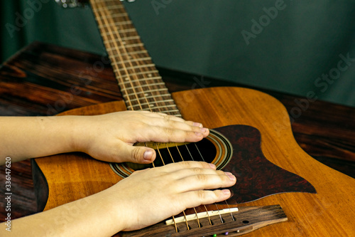 The boy tries to tune and play an acoustic guitar, playing the strings with his fingers.