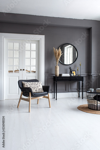 Modern living room interior with stucco molding on the walls with a Scandinavian-style armchair, console, mirror and coffee table.