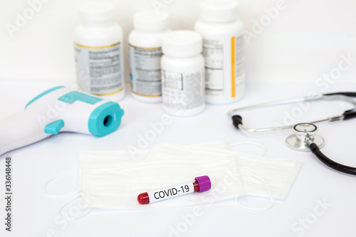 a test tube with a test for the COVID-19 virus lies on a medical mask with tablets and jars of medications on a white table