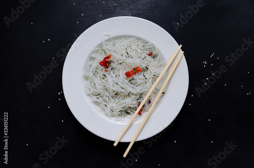 funchose glass rice noodles and bamboo sticks in a large white round plate with sesame seeds ready to eat on a black slate background with place for text. Asian cuisine photo