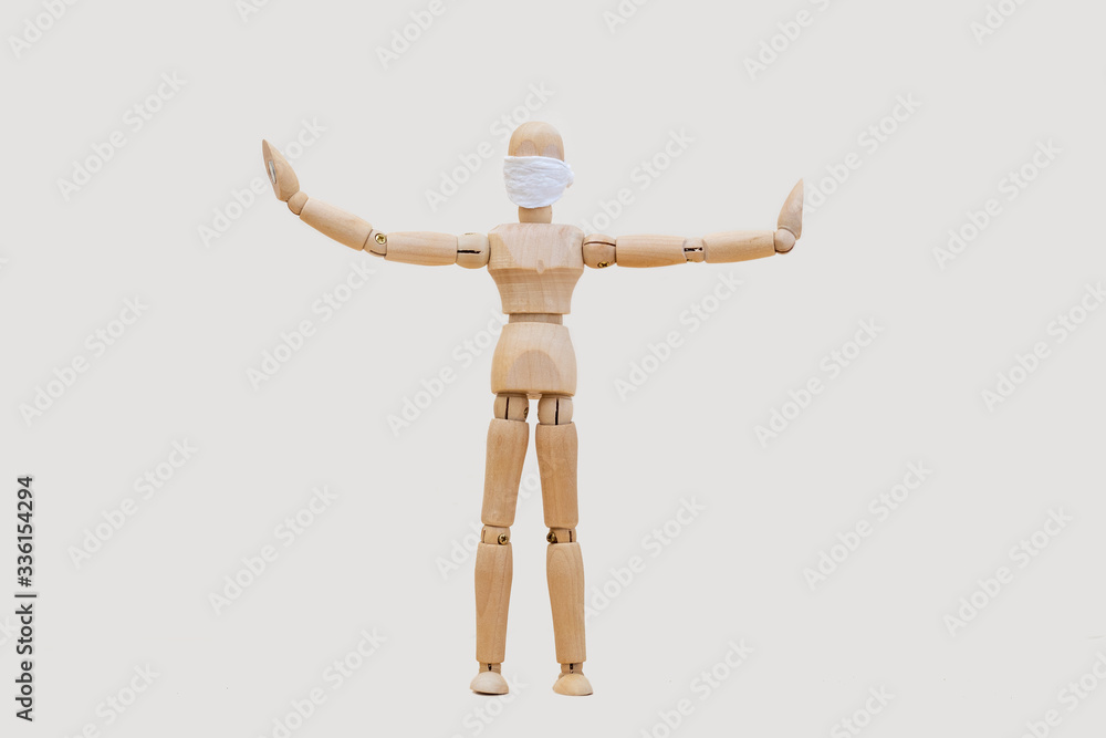 Wooden man mannequin in a protective medical mask holds his hands in different directions standing on a light gray background. Concept - keep your distance during quarantine. Wooden man mannequin in a protective medical mask holds his hands in different directions standing on a light gray background. Concept - keep your distance during quarantine.