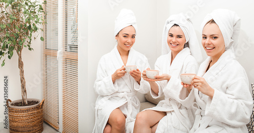 enjoy drinking tea at the spa. Three beautiful women wearing bathrobes and towels on head drinking hot tea and having cool resting