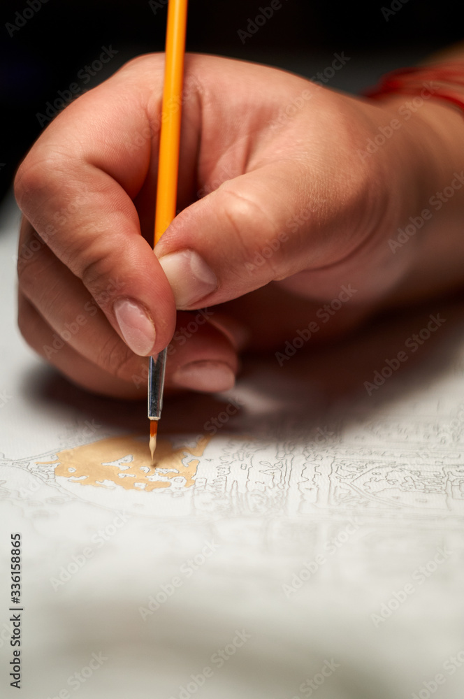 Girl hand draws with a brush painting by numbers on canvas. Creative hobby during the quarantine. Picture by numbers. Girl hand draws with a brush painting by numbers on canvas. Creative hobby during the quarantine. Picture by numbers.