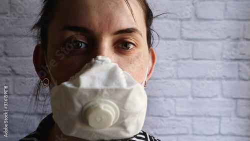 Portrait of a young woman in a mask from a coronavirus epidemic against a white brick wall. Covid-19 health and safety concept, protection against the H1H1 virus. Copy space. excited look photo