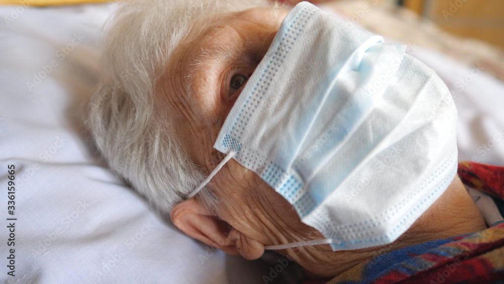 Fototapeta premium Close up face of old woman wearing protective mask from virus. Sick elderly lady with medical face mask lying at bed in hospital. Concept of health and safety life from coronavirus or pandemic