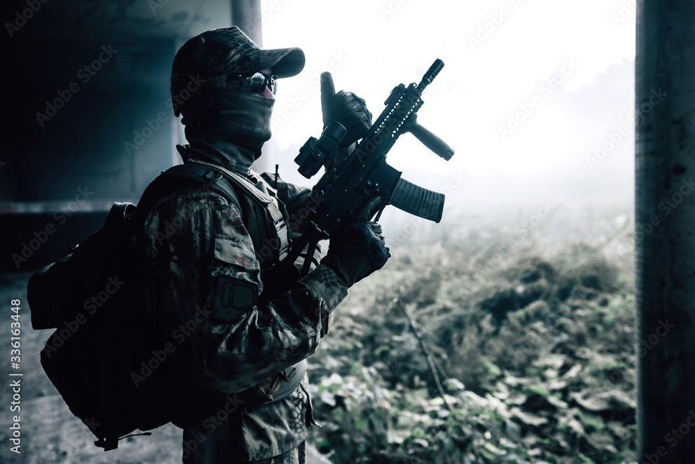 Camouflage soldier standing in a concrete building with a rifle in his hands in the jungle Camouflage soldier standing in a concrete building with a rifle in his hands in the jungle