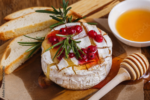 Delicious baked camembert served with berries, rosemary and honey on wooden background.