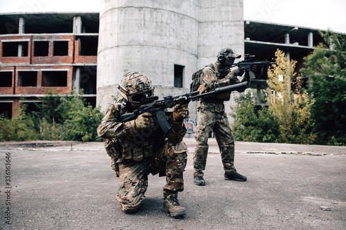 Two armed soldiers in camouflage with rifles storm the building with terrorists