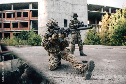 Two armed soldiers in camouflage with rifles on the background of concrete buildings