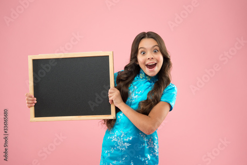 Happy girl hold blackboard pink background. cheerful child hold advertising board. Little schoolchild at lesson. Blackboard for advertising text, copy space. Back to school marketing campaig photo