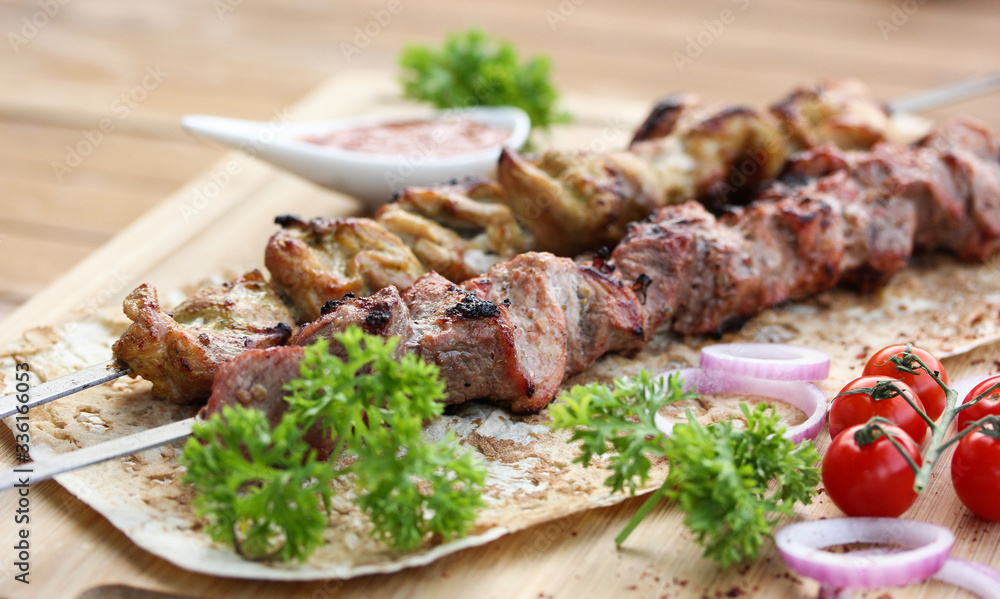 Meat and chicken skewers on pita bread with parsley, onion and cherry tomatoes on a wooden table. Ketchup in a bowl. Picnic. Fried meat on the fire. Background image, copy space