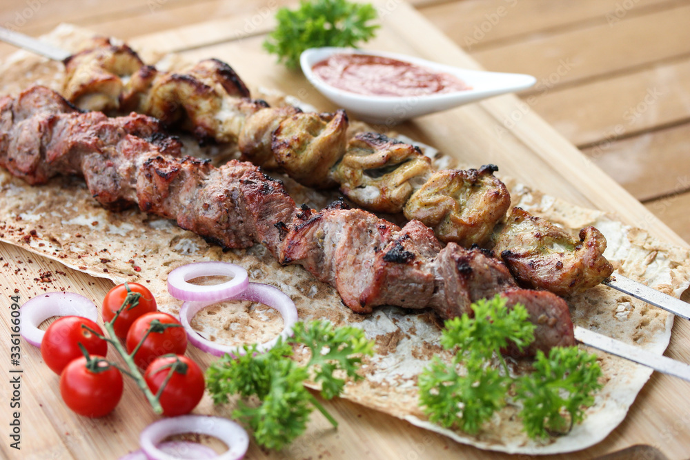 Meat and chicken skewers on pita bread with parsley, onion and cherry tomatoes on a wooden table. Ketchup in a bowl. Picnic. Fried meat on the fire. Background image, copy space Meat and chicken skewers on pita bread with parsley, onion and cherry tomatoes on a wooden table. Ketchup in a bowl. Picnic. Fried meat on the fire. Background image, copy space