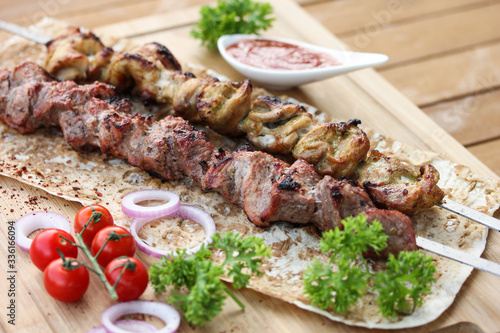 Meat and chicken skewers on pita bread with parsley, onion and cherry tomatoes on a wooden table. Ketchup in a bowl. Picnic. Fried meat on the fire. Background image, copy space