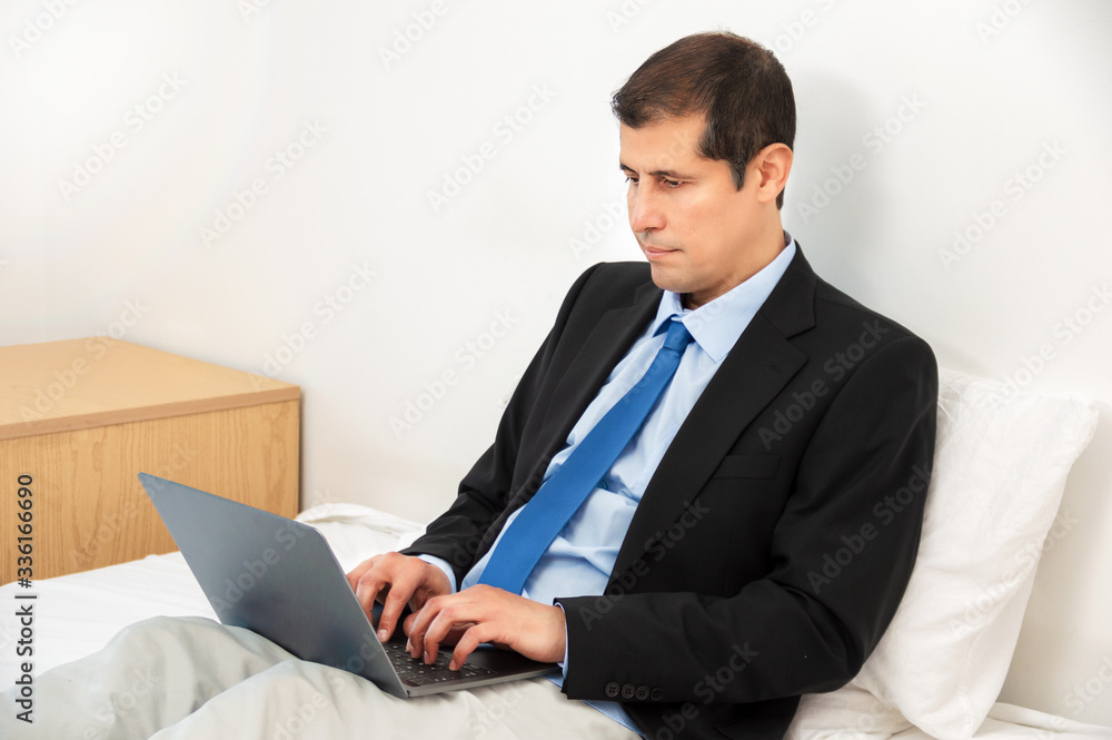Mature business man holding a cup of coffee and working with laptop on bed Mature business man holding a cup of coffee and working with laptop on bed