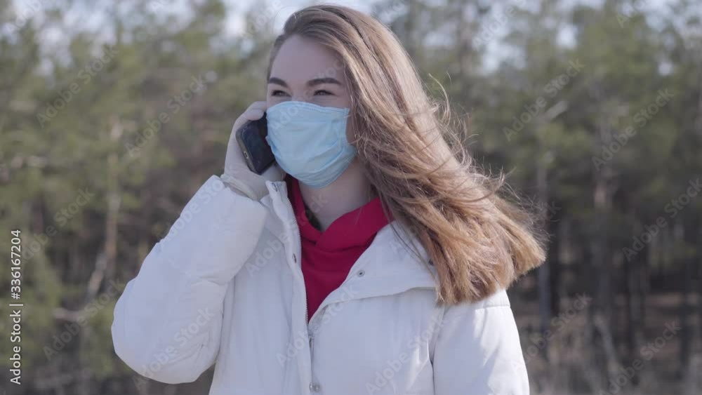 Portrait of brunette young woman in face mask and protective gloves talking on the phone. Brunette Caucasian girl spending sunny spring day alone during Covid-19 quarantine. Coronavirus pandemic. Portrait of brunette young woman in face mask and protective gloves talking on the phone. Brunette Caucasian girl spending sunny spring day alone during Covid-19 quarantine. Coronavirus pandemic.