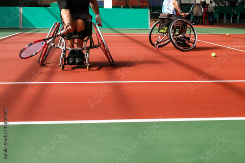 Disabled mature men on a wheelchair playing tennis on an indoor tennis court. Copy space