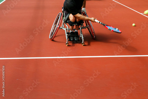Disabled mature man on a wheelchair playing tennis on an indoor tennis court. Copy space