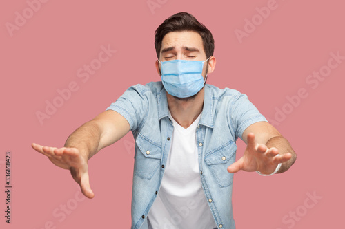 Loneless and blindness. Portrait of lost worry man with surgical medical mask in blue shirt standing with closed eyes and try to touching something or find. indoor shot, isolated on pink background. photo