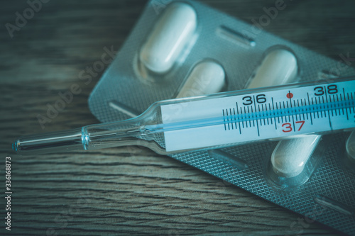 Thermometer and pack of tablets on wooden background