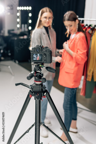 selective focus of digital camera with happy stylist standing with trendy model on screen