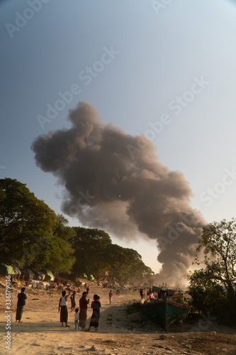 smoke from a burning ship near an asian river in a poor town
