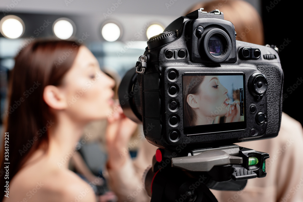 selective focus of digital camera with makeup artist applying lip gloss on beautiful model selective focus of digital camera with makeup artist applying lip gloss on beautiful model
