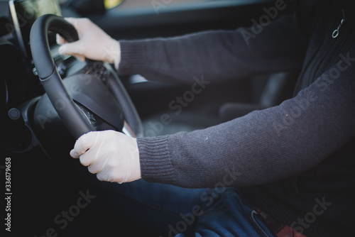 A man driving a car wearing hand gloves as a part of infection protection