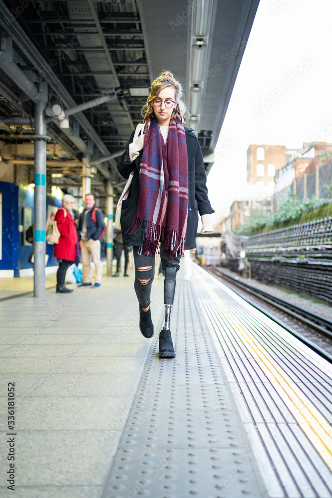 Young woman with leg prosthesis walking at station platfom
