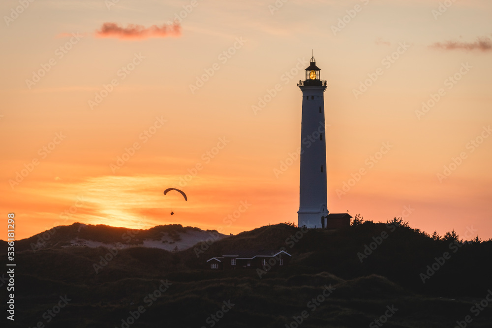 Denmark, Hvide Sande, Lighthouse standing against moody sky at dusk with silhouette of paraglider in background Denmark, Hvide Sande, Lighthouse standing against moody sky at dusk with silhouette of paraglider in background
