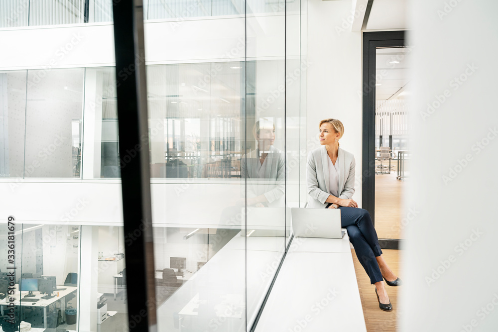 Blond businesswoman with laptop, sitting on windowsill in office building Blond businesswoman with laptop, sitting on windowsill in office building