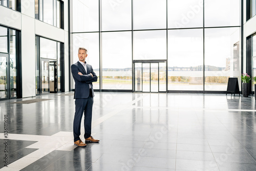 Successful businessman standing in entrance hall of office building, with arms crossed